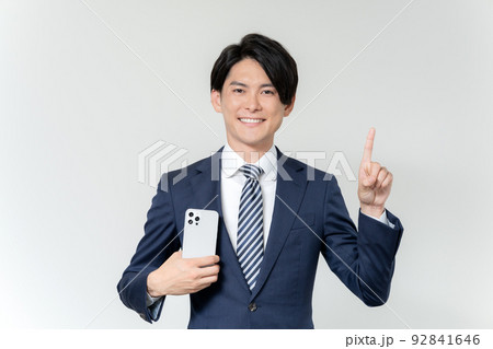 白背景のスマホを持って1番のポーズをする若いビジネスマンのポートレート 白背景のスマホを持って1番のポーズをする若いビジネスマンのポートレート 92841646