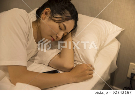 夜、寝室でスマホを見ながら寝てしまった若い女性 92842167