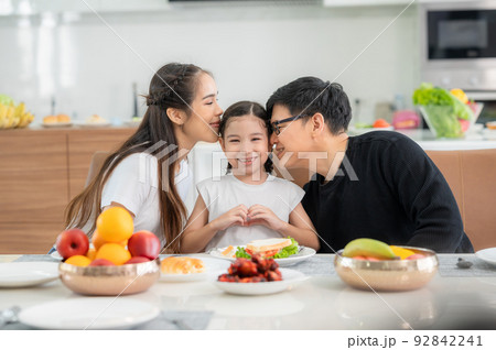 Parents kissing daughter at dinning table in kitchen 92842241