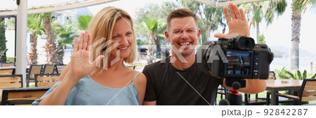 Happy couple waving at the camera on a tripod in a cafe Happy couple waving at the camera on a tripod in a cafe 92842287