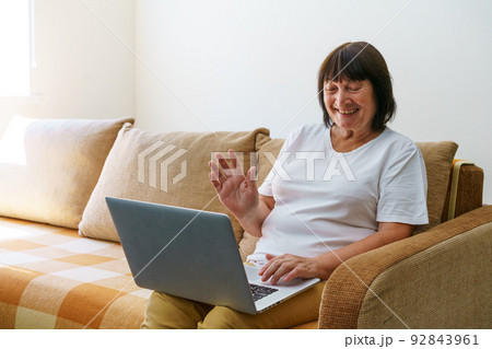 Overjoyed mature woman sitting on sofa in living room talking on video call 92843961