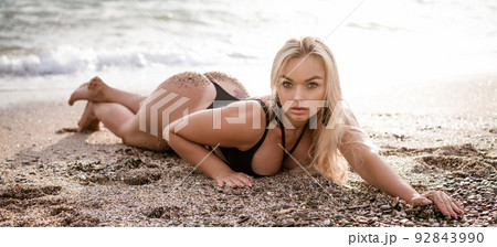 Beautiful young woman sitting posing in a swimsuit on the seashore Beautiful young woman sitting posing in a swimsuit on the seashore 92843990
