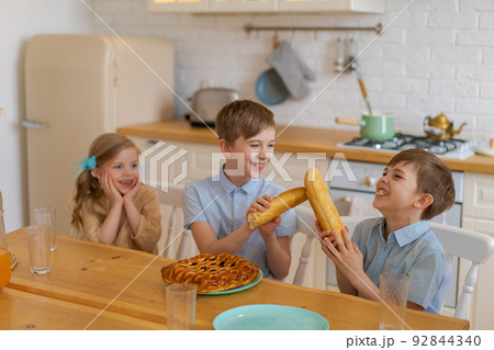 Cheerful children are sitting at table in kitchen, playing with loaf bread 92844340