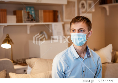 a young guy in a shirt and a protective mask sits on the couch 92844441