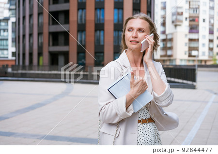 A beautiful blonde girl holds a smartphone and a notebook in her hands. A beautiful blonde girl holds a smartphone and a notebook in her hands. 92844477