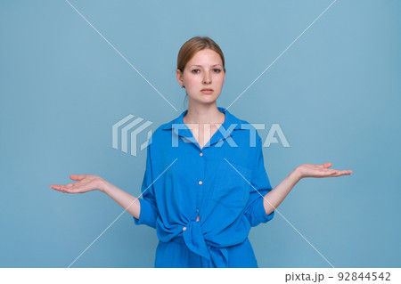 Young woman in shirt on blue background, pointing to side with both hands Young woman in shirt on blue background, pointing to side with both hands 92844542