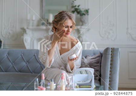 Pretty european woman applies facial cream on her face holds jar cosmetic Pretty european woman applies facial cream on her face holds jar cosmetic 92844875