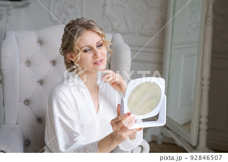 Women's skin care. Caucasian woman touches her face and looks in mirror 92846507