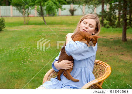 Happy woman in blue dress holding ginger imitation cat outside, outdoors Happy woman in blue dress holding ginger imitation cat outside, outdoors 92846663