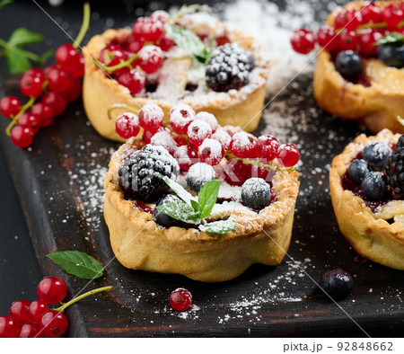 Fruit tart with red currants sprinkled with powdered sugar on a black table Fruit tart with red currants sprinkled with powdered sugar on a black table 92848662