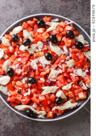 Cod esqueixada salad with tomatoes, onion and olive close-up in a plate. Vertical top view 92849679