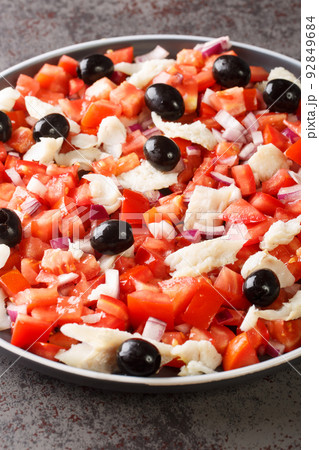 Cod esqueixada salad with tomatoes, onion and olive close-up in a plate. Vertical 92849684