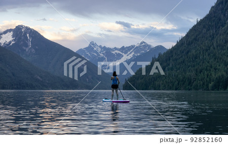 Adventurous Woman Paddle Boarding in a Lake around Canadian Mountain Landscape 92852160