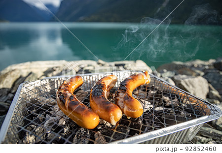 Grilling sausages on disposable barbecue grid. 92852460