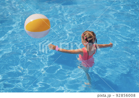 A girl in a pink swimsuit runs after an inflatable ball in the swimming pool. Water games at the aquapark 92856008