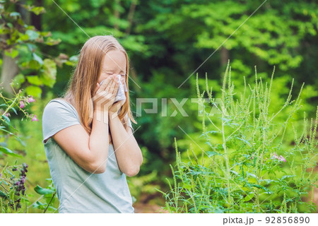 Young woman sneezes because of an allergy to ragweed Young woman sneezes because of an allergy to ragweed 92856890