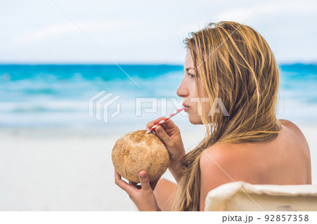 Young woman drinking coconut milk on Chaise-longue on beach. 92857358