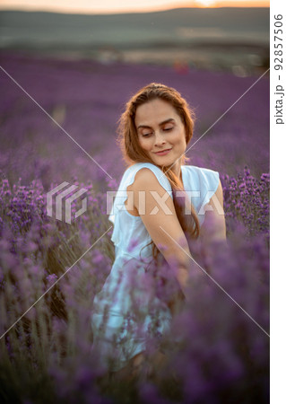 A beautiful girl in a white dress and loose hair on a lavender field. Beautiful woman in a lavender field at sunset. Soft Focus 92857506