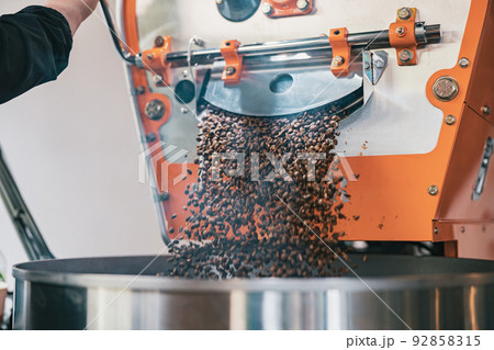 Close up of Business owner pouring roasted coffee beans from large roaster into cooling cylinder Close up of Business owner pouring roasted coffee beans from large roaster into cooling cylinder 92858315