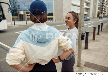 Two sportive young female friends walking city after morning running Two sportive young female friends walking city after morning running 92858579