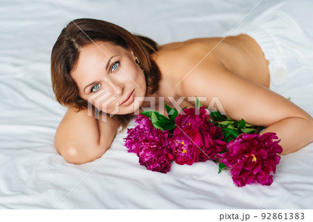 attractive brunette topless woman with a bouquet of peonies on the bed. 92861383