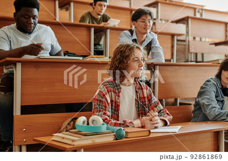 Youthful girl in casualwear listening to teacher while sitting by desk 92861869