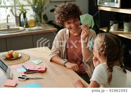 Happy young woman showing her youthful daughter green paper origami Happy young woman showing her youthful daughter green paper origami 92862092