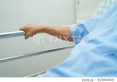 Asian elder senior woman patient holding bed rail while lie down with hope waiting her family in hospital. 92868800