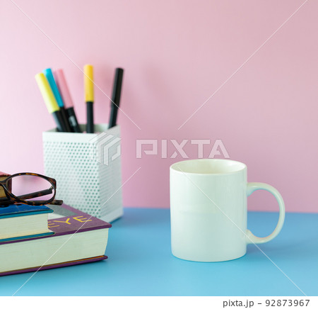 Back to school concept, white mug on blue table with pink wall. Girly and feminine decoration style. Back to school concept, white mug on blue table with pink wall. Girly and feminine decoration style. 92873967