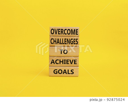 Challenges or goals symbol. Wooden blocks with words 'Overcome challenges to achieve goals'. Beautiful yellow background. Business and 'Overcome challenges to achieve goals' concept. Copy space. Challenges or goals symbol. Wooden blocks with words 'Overcome challenges to achieve goals'. Beautiful yellow background. Business and 'Overcome challenges to achieve goals' concept. Copy space. 92875024