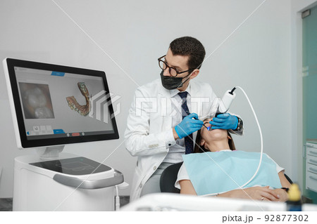 Male orthodontist scaning patient with dental intraoral scanner and controls process on screen. 92877302