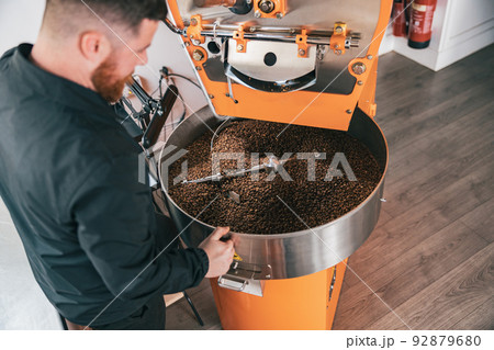 Professional barista operating modern coffee bean roasting machine 92879680