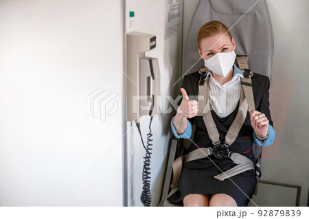 Stewardess in medical mask sitting in chair in airplane cabin 92879839