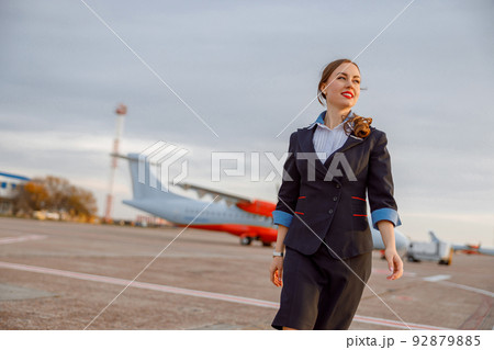 Cheerful female flight attendant walking down airfield Cheerful female flight attendant walking down airfield 92879885