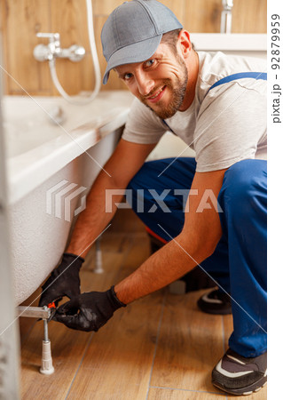 Cheerful plumber or technician smiling at camera while installing a bathtub in bathroom 92879959