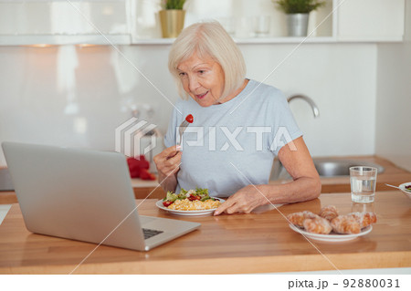Concentrated senior woman eating breakfast at home Concentrated senior woman eating breakfast at home 92880031