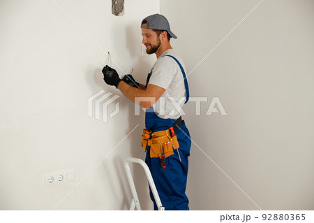 Busy handyman electrician holding screwdriver while working on residential electric system 92880365