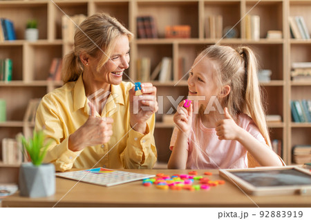 Friendly speech therapist curing child's problems, cute girl learning letters R and U with private tutor Friendly speech therapist curing child's problems, cute girl learning letters R and U with private tutor 92883919