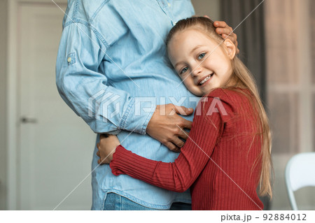 Pretty little girl hugging her pregnant mother big belly and smiling at camera, kid bonding with expecting mom Pretty little girl hugging her pregnant mother big belly and smiling at camera, kid bonding with expecting mom 92884012