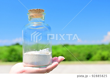 サンゴ砂とサンゴが入っているガラス瓶を持つ手　SDGs  環境問題　イメージ 92885825