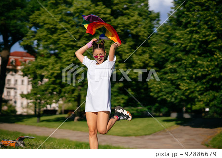 Young woman waving LGBT pride flag in the park. 92886679