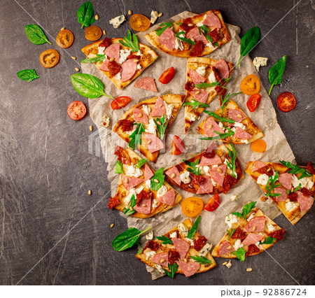 Cut into slices delicious fresh pizza with sausage and cheese on a dark background. Top view with copy space for text. Pizza on the black concrete table. flat lay 92886724