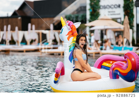 Woman on inflatable unicorn toy mattress float in pool. 92886725