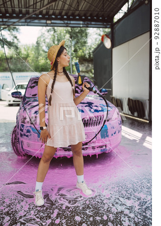 Young woman hose stands in front of a car covered in pink foam 92887010