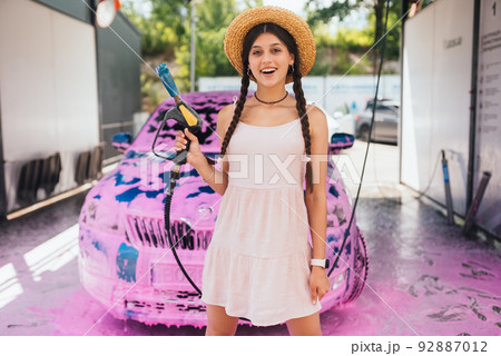 Young woman hose stands in front of a car covered in pink foam 92887012