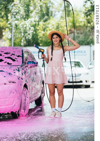 Woman with hose stands by car covered in pink foam 92887013