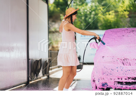 Brunette from a high-pressure hose applies a cleaner on the car Brunette from a high-pressure hose applies a cleaner on the car 92887014