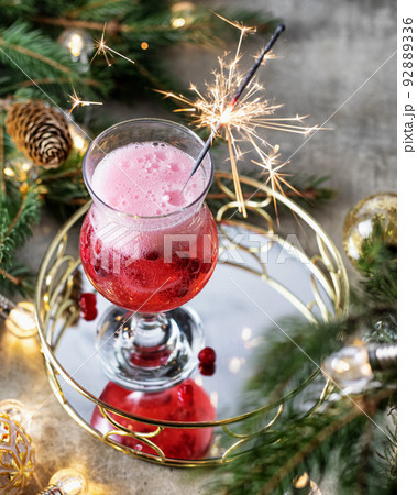 Festive champagne cocktail and a burning sparkler against the background of fir branches and garland lights. Merry christmas concept 92889336