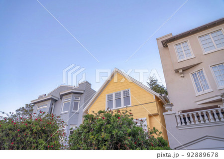 Yellow gable house in the middle of two houses with painted concrete wall exterior 92889678