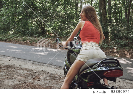 Young woman biker in a helmet sitting on a motorcycle in the underground parking garage Young woman biker in a helmet sitting on a motorcycle in the underground parking garage 92890974